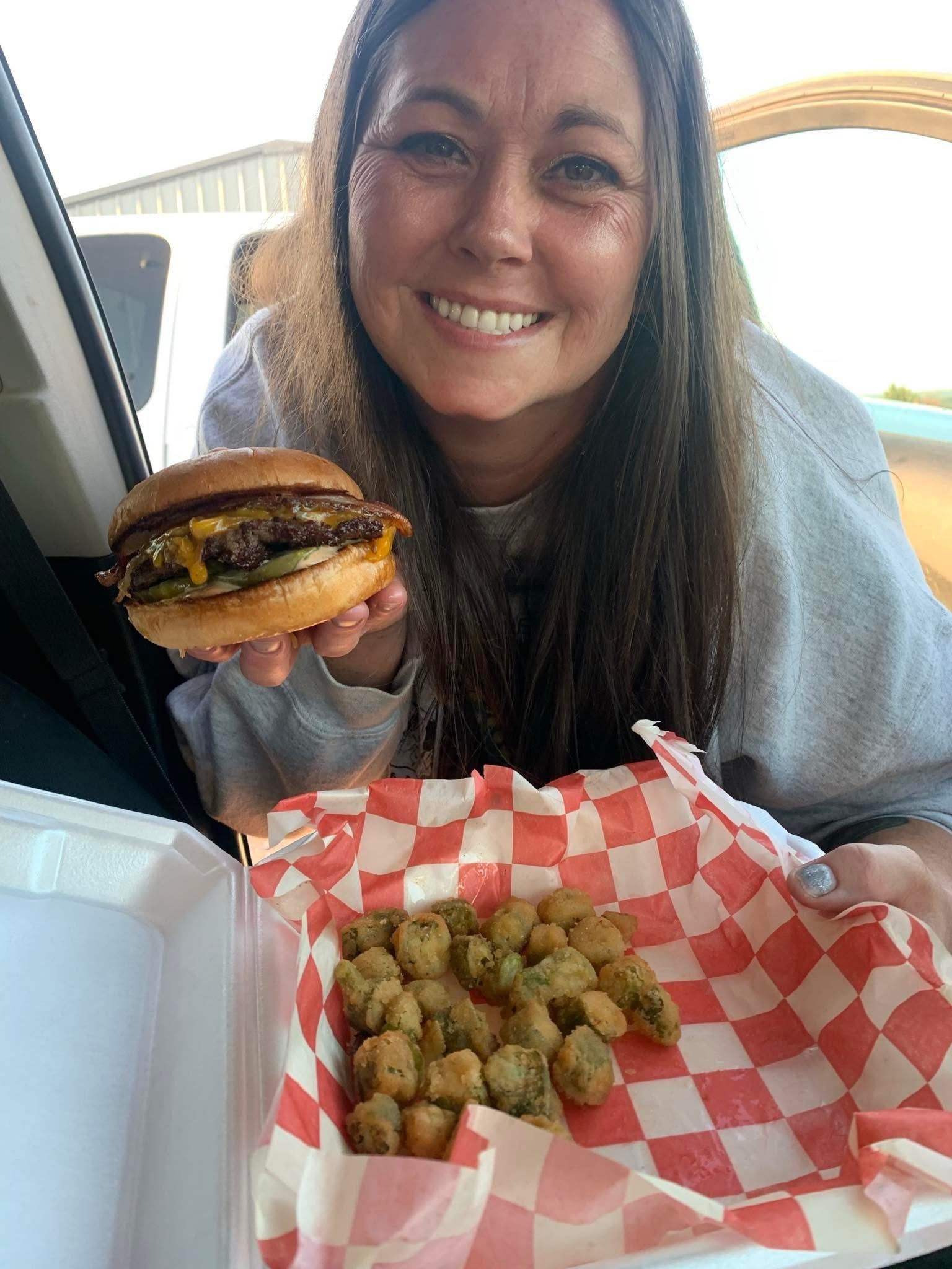 Happy customer holding freshly made onion burger with fried okra in trailer takeout container
