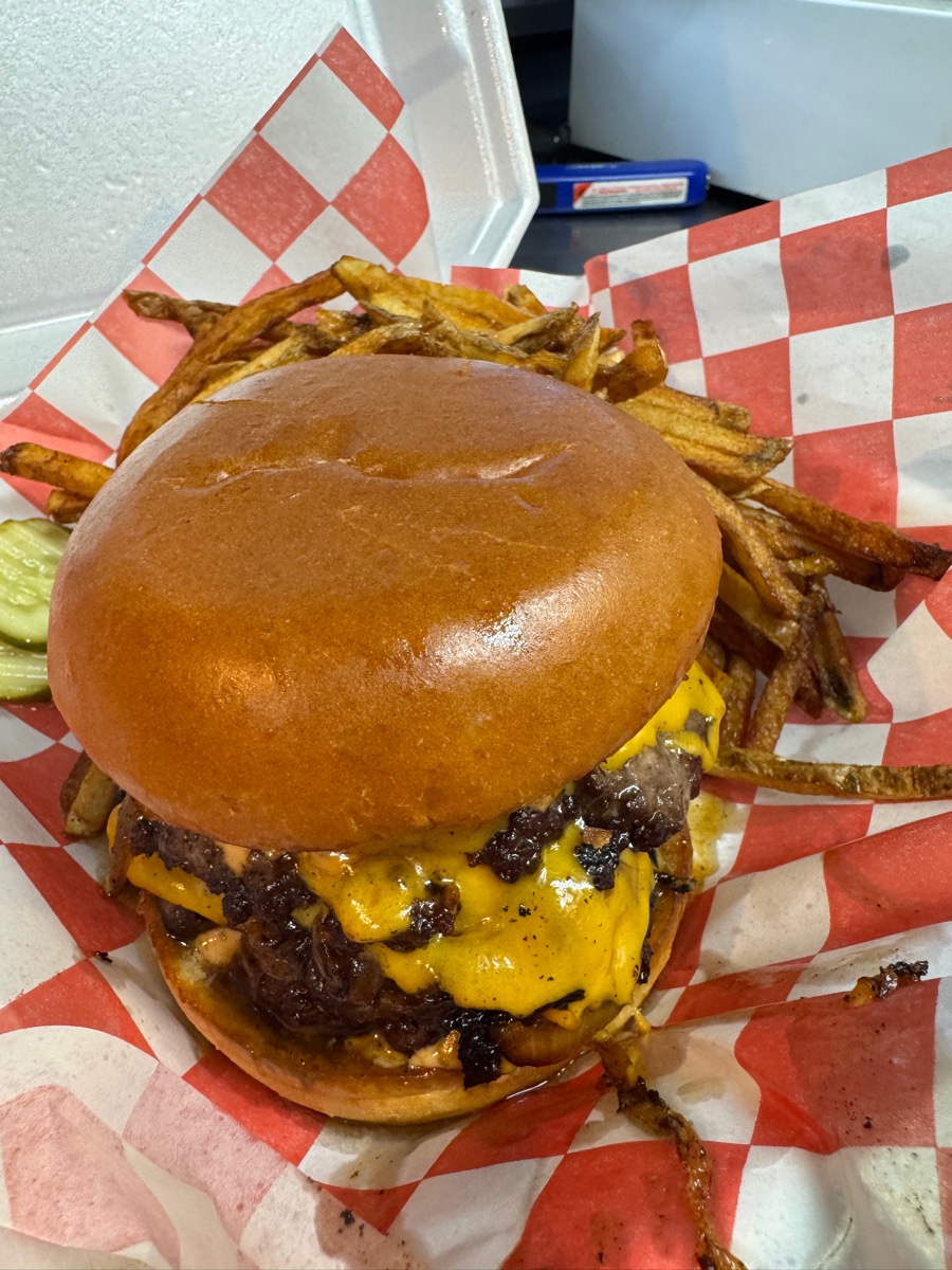 Close-up overhead view of Burger Nation freshly grilled Double Onion Burger on red checkered paper with hand-cut fries